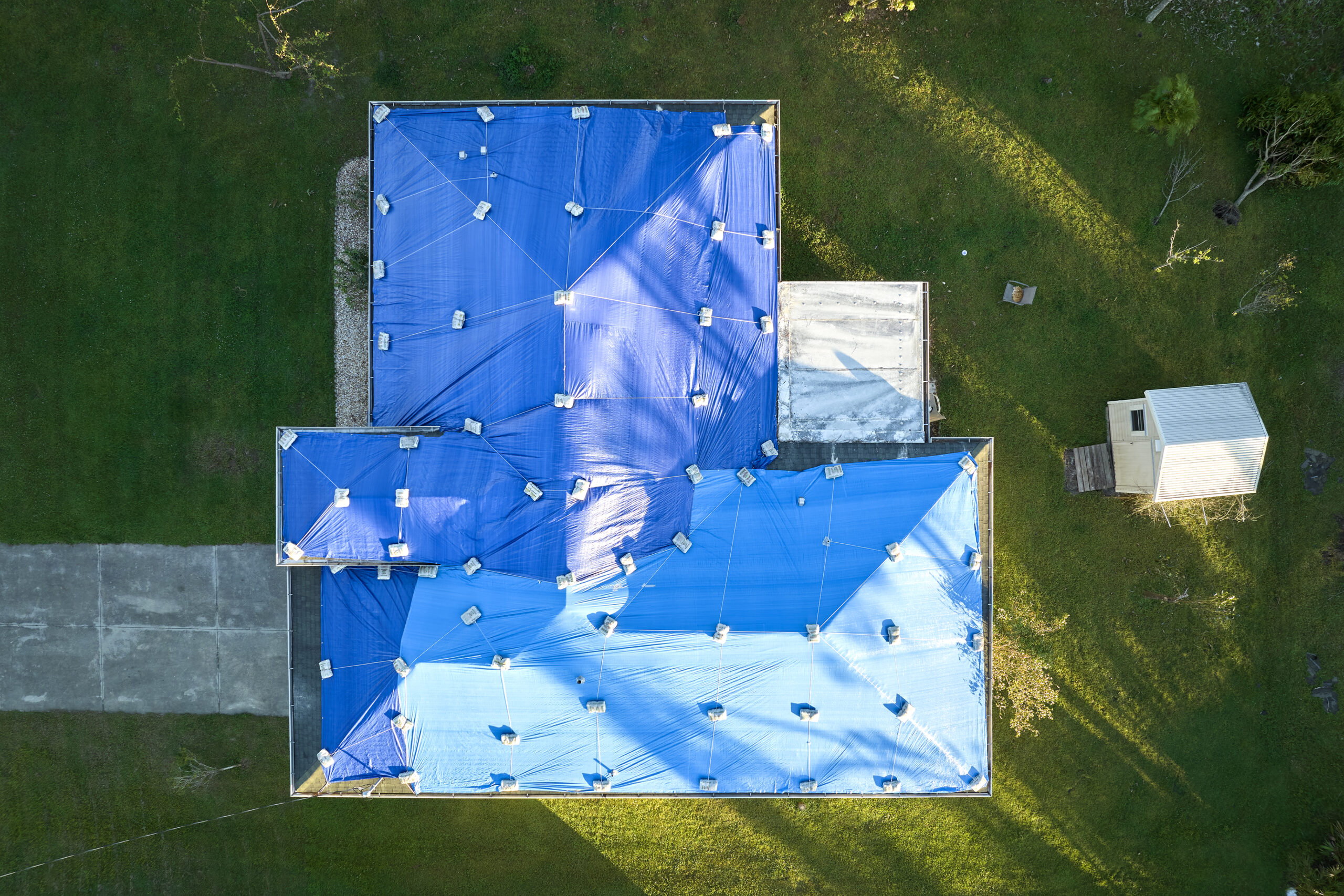 Hurricane Ian damaged house rooftop covered with protective plastic tarp against rain water leaking until replacement of asphalt shingles. Aftermath of natural disaster.